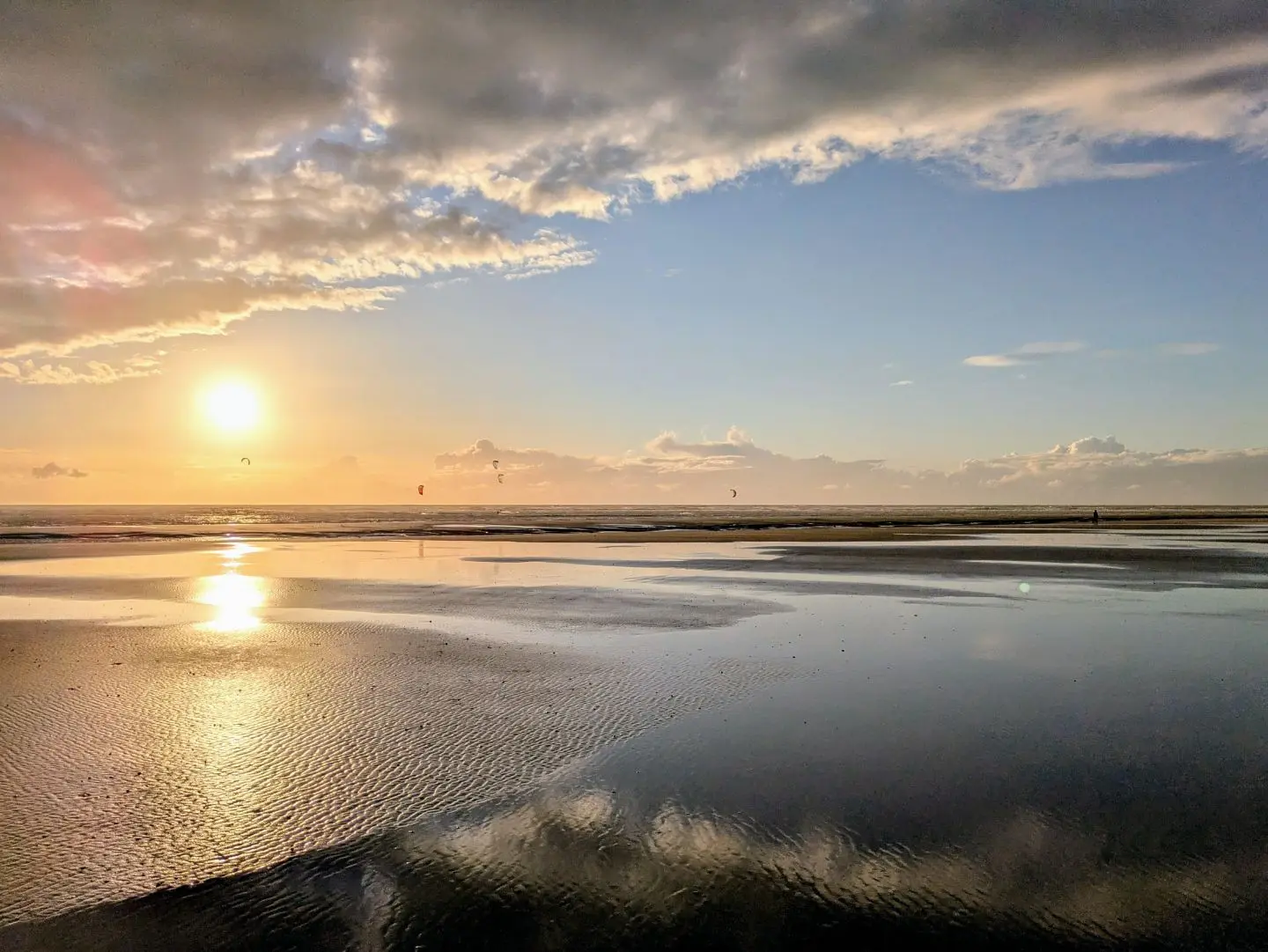 Sonnenuntergang über ruhigem Meer mit reflektierendem Wasser und vereinzelten Wolken am Himmel.