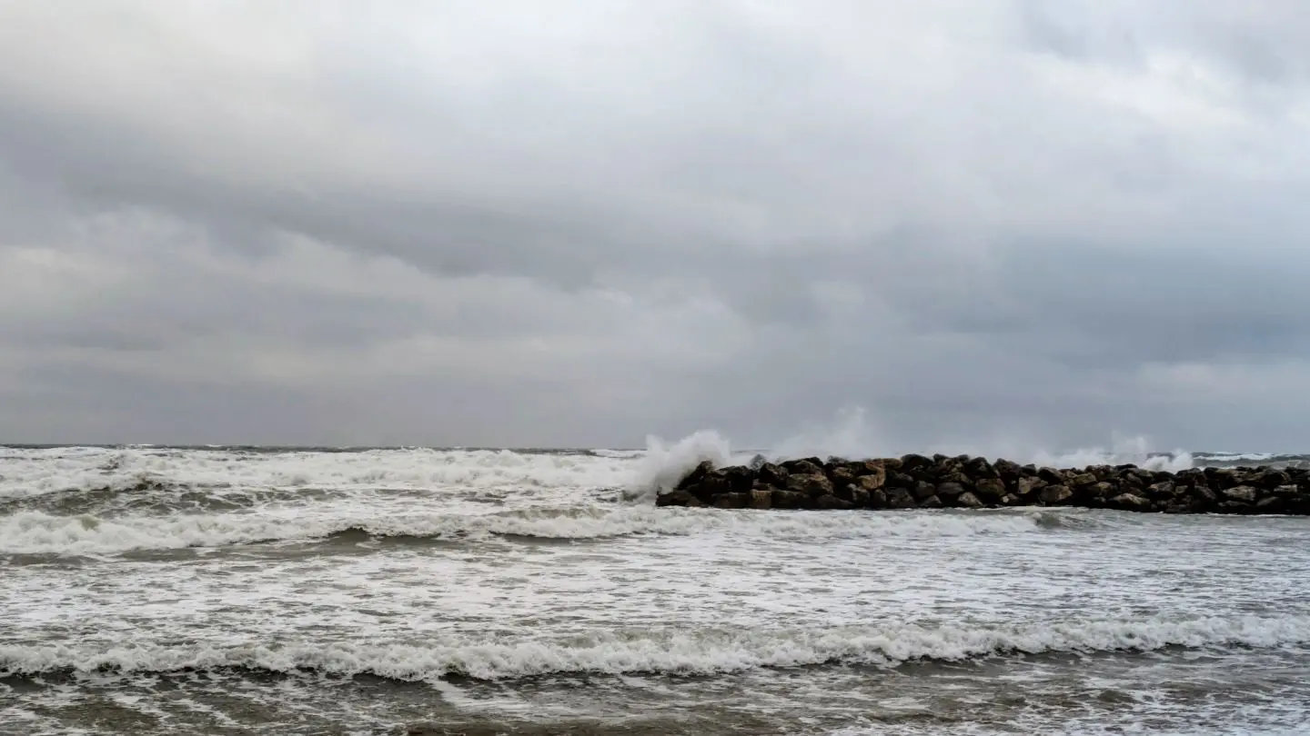 Wellen schlagen gegen eine Felsmole unter bewölktem Himmel am Meer.
