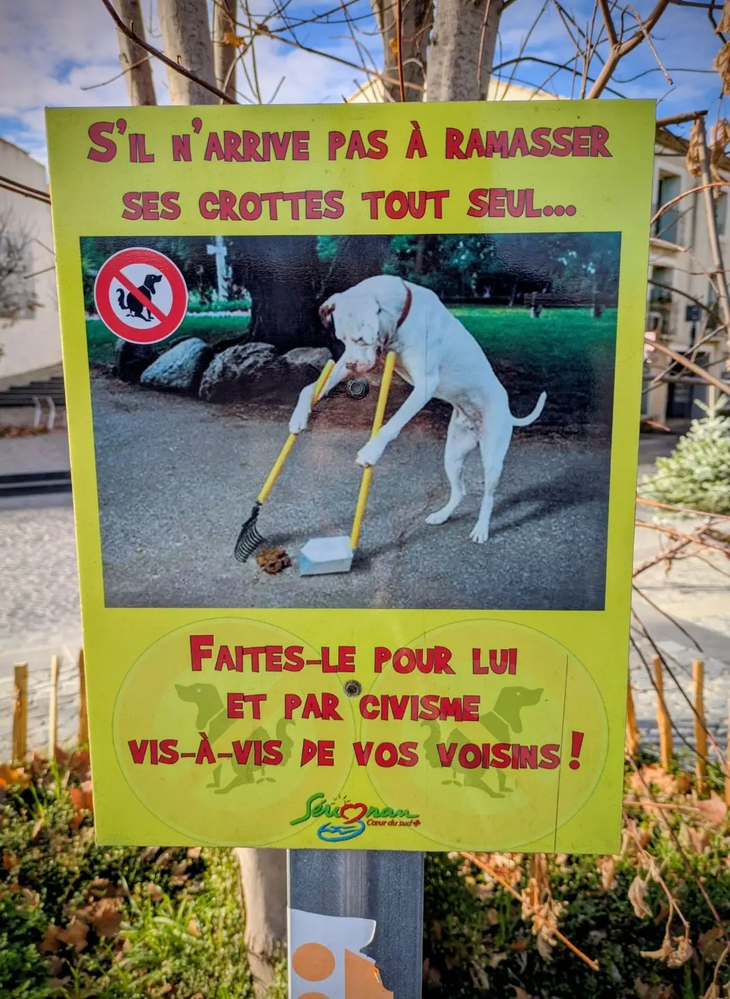 Schild mit Foto eines Hundes, der mit zwei Greifzangen Hundekot aufnimmt, und französischem Text, der zur Sauberkeit im Viertel auffordert.
