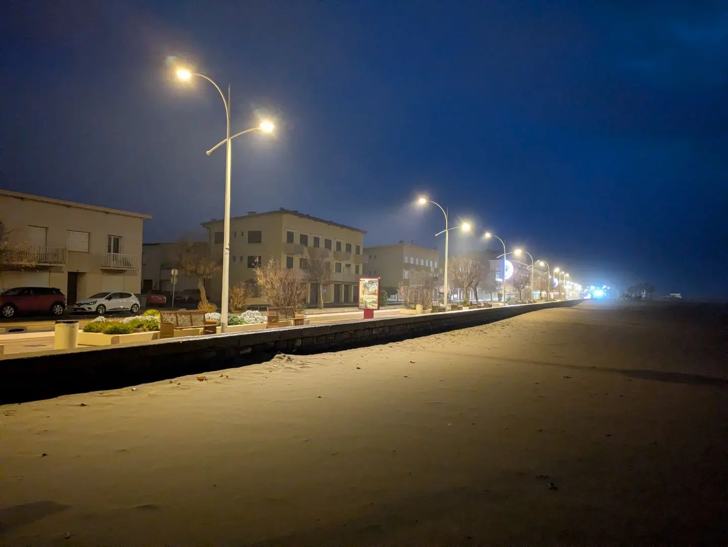 Straße mit beleuchteten Straßenlaternen und Häusern bei Nacht unter dunklem Himmel.