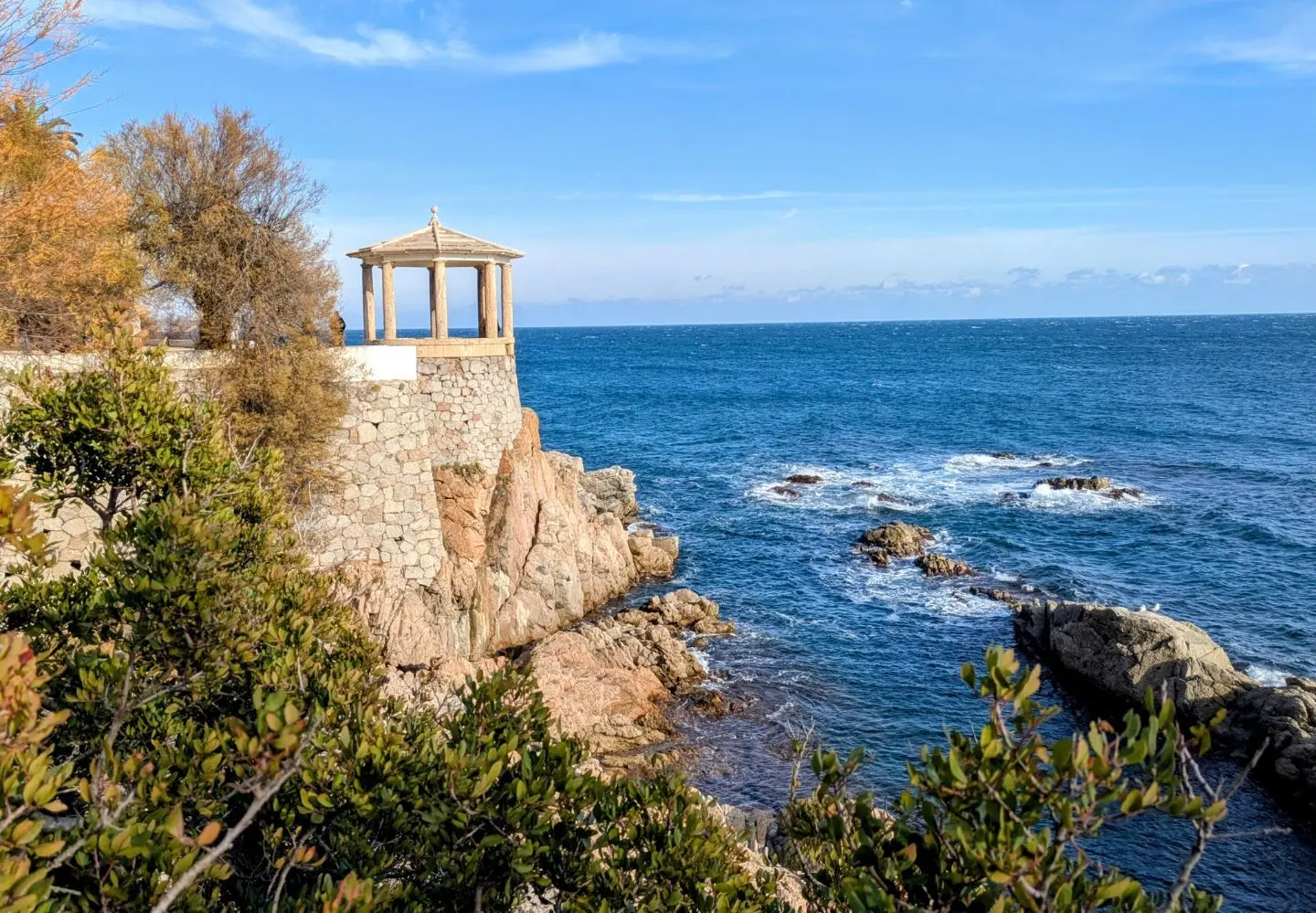 Kleiner Pavillon auf einer Felsklippe mit Blick auf das Meer, umgeben von Büschen und Bäumen