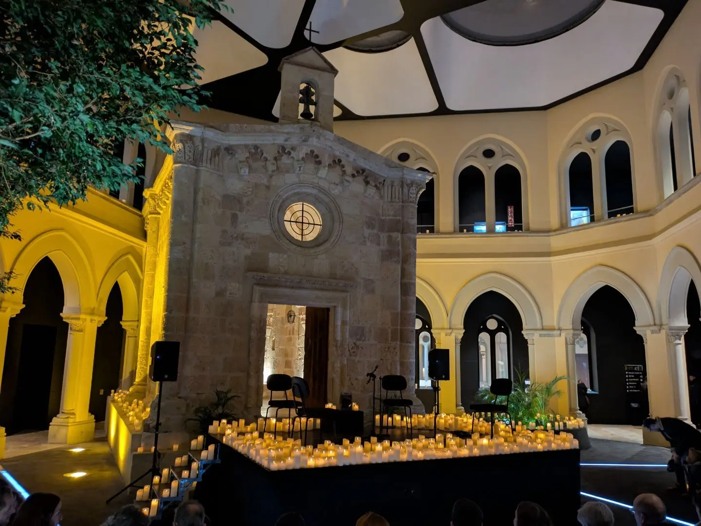 Innenraum einer Kirche mit einer kleinen Kapelle in der Mitte, umgeben von zahlreichen Kerzen auf einem Podest und Stühlen, beleuchtet durch warmes Licht.