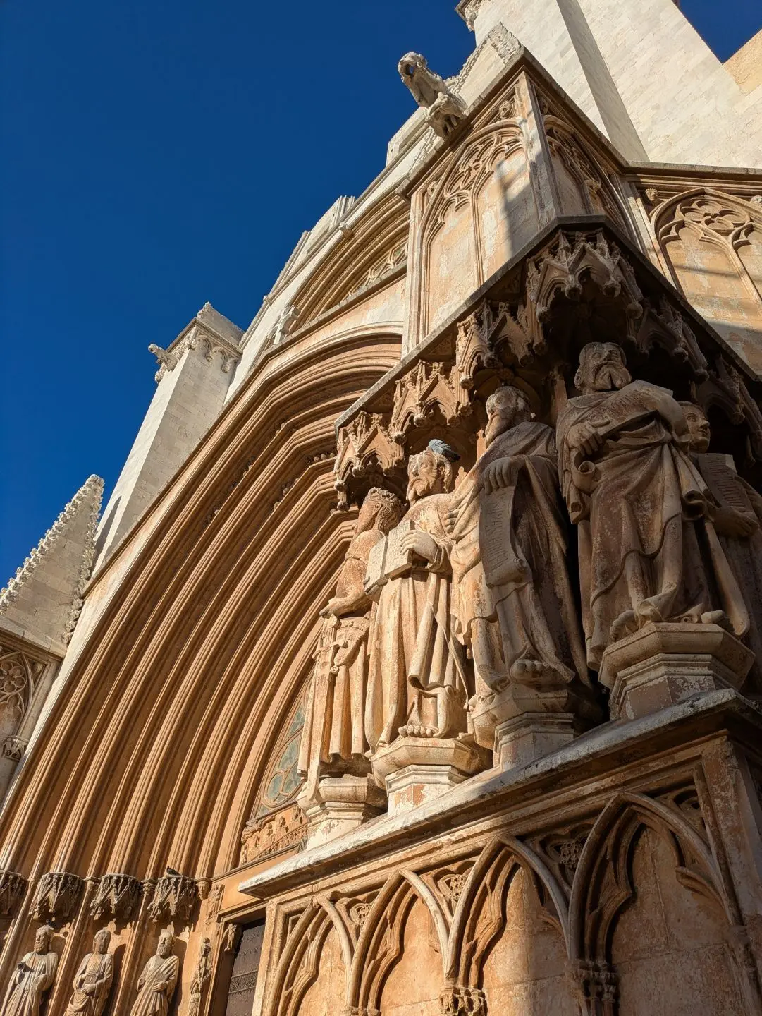 Nahaufnahme von steinernen Figuren an der Fassade eines gotischen Gebäudes vor blauem Himmel.