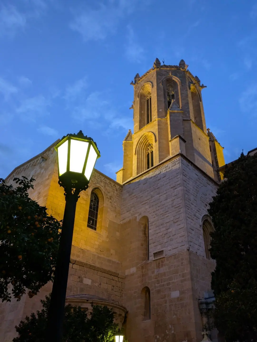 Kirchturm eines historischen Gebäudes bei Abenddämmerung mit beleuchtetem Laternenmast im Vordergrund.