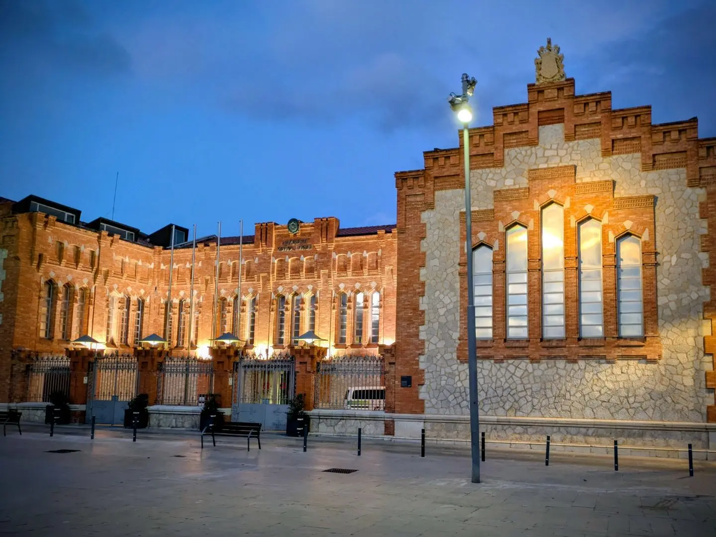 Beleuchtetes historisches Backsteingebäude mit großen Fenstern und steinverkleideter Fassade bei Dämmerung.